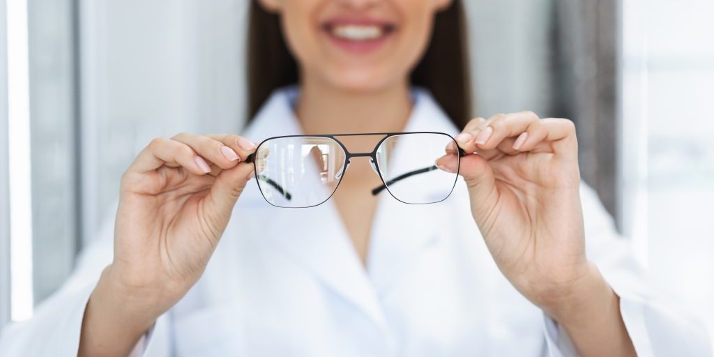 Eyesight And Vision Concept. Closeup of unrecognizable optician showing new eyeglasses to camera, standing at optics store, blurred background, selective focus on eyewear. Woman offering specs
